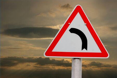 Road turns left traffic sign against stormy skyの写真素材
