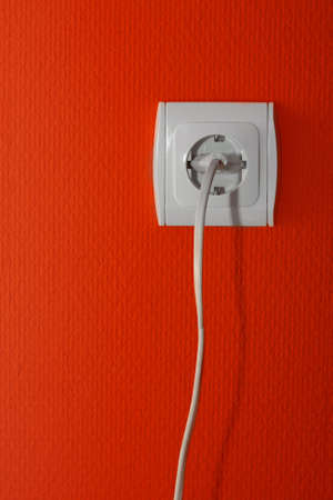 Electric outlet on a red wall, cable connectedの写真素材