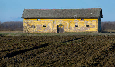 Old, ruined barn on a farmland with plowed fieldsの写真素材
