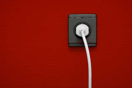 Electric outlet on red wall with cable connectedの写真素材