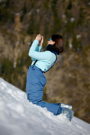 Female skier taking photos in the snowの写真素材
