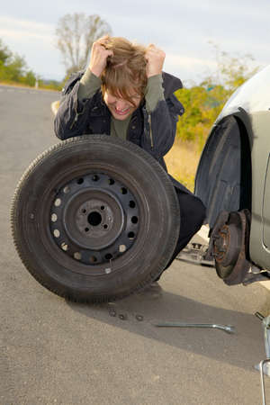 Frustrated man changing wheel on a carの写真素材