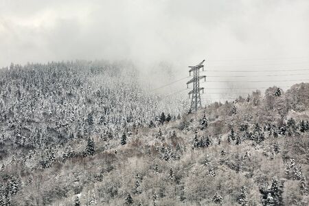 Power line in winter, big, high voltage pylon on minimalist, snowy mountain landscapeの写真素材