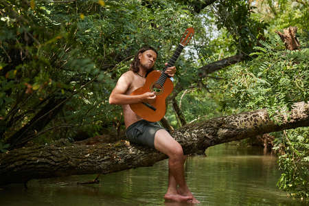 Playing the guitar on a tree above a riverの写真素材