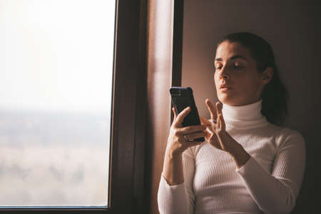 Cheerful girl in a white turtleneck talking at home on the phone. High quality photoの写真素材