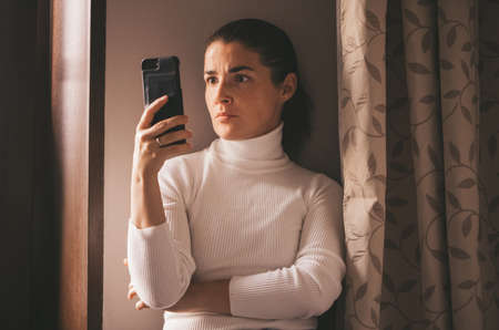 Cheerful girl in a white turtleneck talking at home on the phoneの写真素材