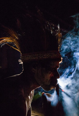 INDONESIA, IRIAN JAYA, ASMAT PROVINCE, JOW VILLAGE - JUNE 12: Asmat tribe man smokes in the dark.