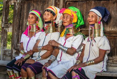 Four Padaung women in traditional dress and with metal rings around their neck are sitting next to...