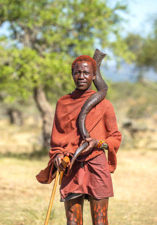 Young Masai warrior is standing in the savannah in traditional clothes and with a ritual horn in his hands. Tanzania, East Africa, August 12, 2018.のeditorial素材