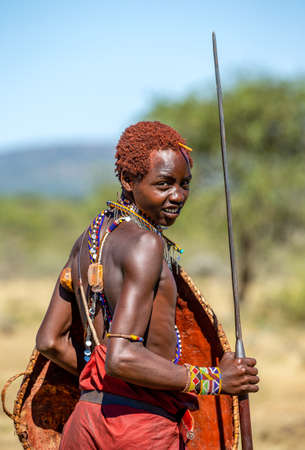 Young Masai warrior is standing in the savannah in traditional clothing with a spear and a shield in his hands. Tanzania, East Africa, August 12, 2018.のeditorial素材