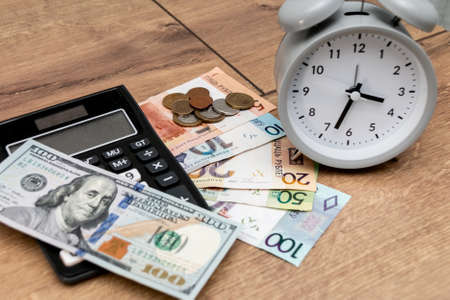 Banknotes and coins of the Republic of Belarus, one hundred US dollars, an alarm clock and a calculator on a wooden background. Belarusian monetary inflation. Time to change money.の写真素材