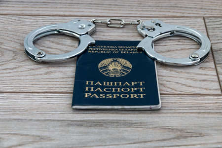 Passport proving the identity of a citizen of the Republic of Belarus and steel handcuffs on a wooden background. close-up.の写真素材