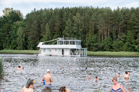 Minsk. Belarus. 07.27.2022. The ship in the form of a two-storey houseboat floats near the people having a rest and bathing in the river. summer outdoor recreation.の写真素材