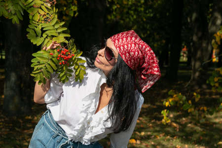 A girl in glasses and a scarf holds a rowan branch in an autumn park. autumn mood.の写真素材