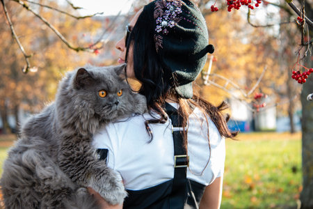 Girl holds a cat on a shoulder against a background of yellow autumn leaves and red rowan. autumn...