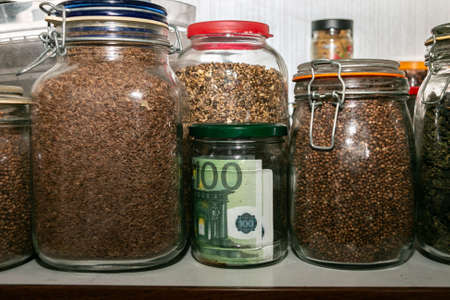 Euro banknotes in a glass jar among other jars with cereals and dried fruits. Keeping money in a glass jar. financial reserves. Secret piggy bank. Money saving concept. Keeping cash at home.の写真素材