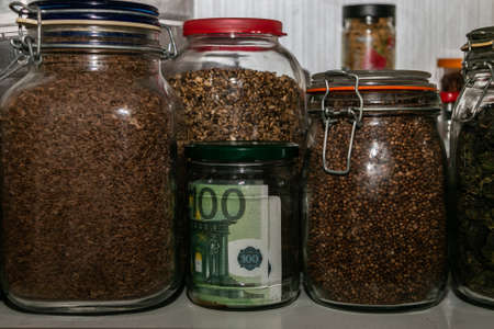 Euro banknotes in a glass jar among other jars with cereals and dried fruits. Keeping money in a glass jar. financial reserves. Secret piggy bank. Keeping cash at home. Money saving concept.の写真素材