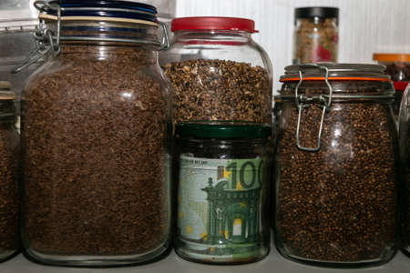 Euro banknotes in a glass jar among other jars with cereals and dried fruits. Keeping money in a glass jar. financial reserves. Keeping cash at home. Money saving concept. Secret piggy bank.の写真素材