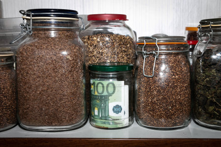 Euro banknotes in a glass jar among other jars with cereals and dried fruits. Keeping money in a glass jar. financial reserves. Keeping cash at home. Money saving concept. Secret piggy bank.の写真素材