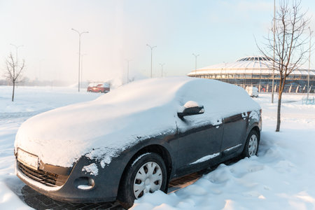 The car in the parking lot is covered with snow. under the snow. Consequences of heavy snowfall. Concept of snowy weather, snowfall, bad winter weather conditions, the effects of a blizzard.の写真素材