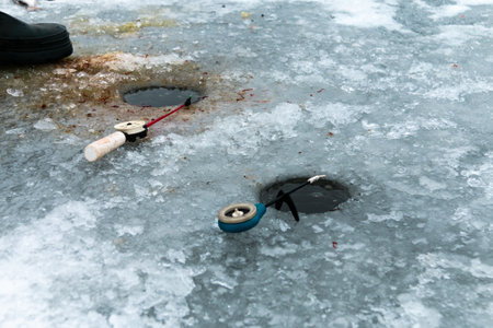 Two winter fishing rods lie on holes drilled in the ice. Winter fishing on the pond. close-up.の写真素材