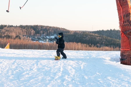 logoisk. Belarus. 07/01/2023. A teenage snowboarder descends the slope of a snow-covered mountain in special equipment. Snowboard - descent at high speed on prepared slopes.の写真素材
