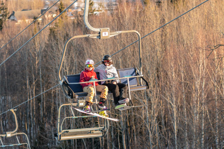 logoisk. Belarus. 07/01/2023. Teenage snowboarders in special equipment ride a chair lift uphill. Winter extreme sport. winter holidays. Ski resort in Belarusのeditorial素材