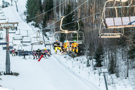 logoisk. Belarus. 10/01/2023. Teenage snowboarders in special equipment ride a chair lift uphill. Winter extreme sport. winter holidays. Ski resort in Belarusのeditorial素材