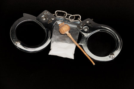 Handcuffs, a bag of white powder and handcuffs on a black background. The concept of punishment for the manufacture and distribution of drugs.の写真素材