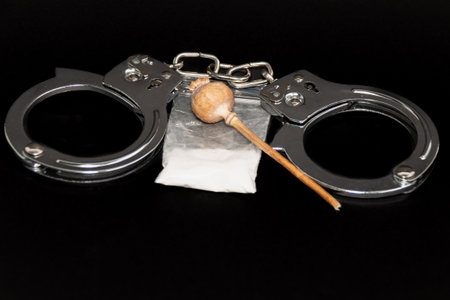 Handcuffs, a bag of white powder and handcuffs on a black background. close-up. The concept of punishment for the manufacture and distribution of drugs.の写真素材