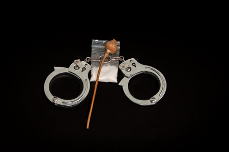 Handcuffs, a bag of white powder and handcuffs on a black background. The concept of punishment for the manufacture and distribution of drugs. close-up.の写真素材
