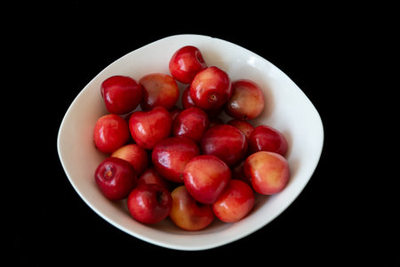 Fresh ripe cherries in a white plate on a black background. Vegetarian breakfast. Health food.の写真素材
