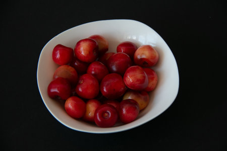Fresh ripe cherries in a white plate on a black background. Health food. Vegetarian breakfast.の写真素材