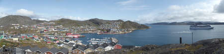 View from one of the many hills of Qaqortog, Iceland, towards the colorful houses of the city, on the right the fjord with an anchored cruise shipの写真素材