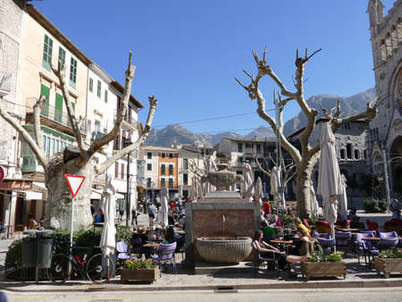 The sprawling Placa Constitucio (Constitution square) in Soller, Mallorca, Balearic Islands, Spain, with a fountain in the center and the mountains of the Serra de Tramuntana in the backgroundのeditorial素材