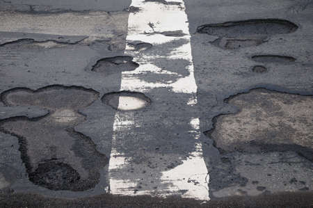 Potholes Damaged road with potholes and a white dividing lineの写真素材