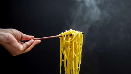 Hand uses chopsticks to pick up tasty noodles in bowl, selective focus. Asian meal, junk food conceptの写真素材