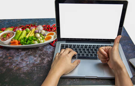 Hand on Laptop isolated white screen over beautiful food, Chilli shrimp paste with fresh vegetable on wood table, to share on social media, social market.の写真素材