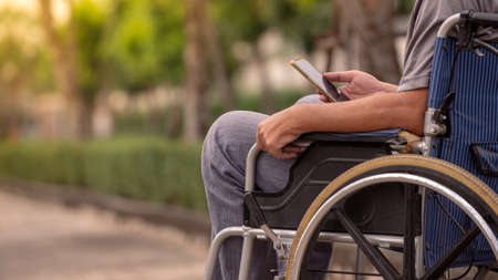 Close-up of a disabled man in a wheelchair using a smartphone.の写真素材