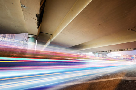 High-speed vehicles bright light trails on urban roads under the overpass at night 