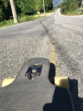 A skateboard on top of a hill over the asphalt on a sunny day