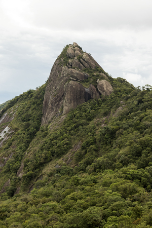 vertical view of a mountain rock face with some trees under white cloudy -  pico e serra do lopoの写真素材