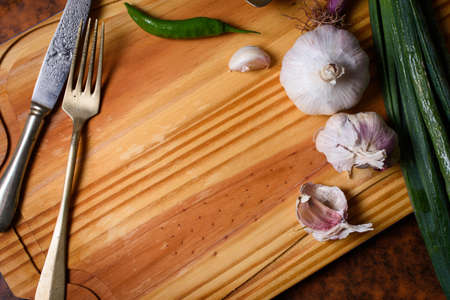 Wooden board with chili, garlic, green onion and vintage cutlery. Graphic resource with vegetarian motif to write in negative spaceの写真素材