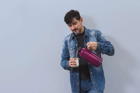 Man priming mate with embroidered colored tumbler dressed in denim on isolated light blue backgroundの写真素材