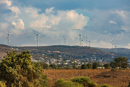 Wind farm. Among farms and hills, wind turbines emerge as a symbol of clean energy, converting the kinetic energy of the wind into electricity.の写真素材