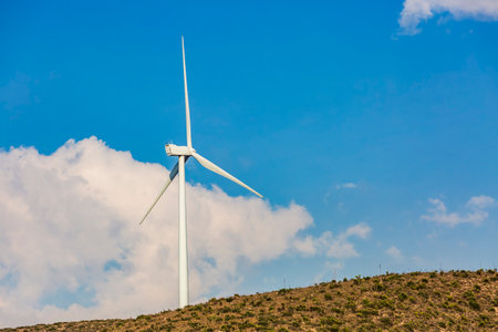 Wind farm. Among farms and hills, wind turbines emerge as a symbol of clean energy, converting the kinetic energy of the wind into electricity.の写真素材