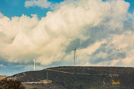 Wind farm. Among farms and hills, wind turbines emerge as a symbol of clean energy, converting the kinetic energy of the wind into electricity.の写真素材