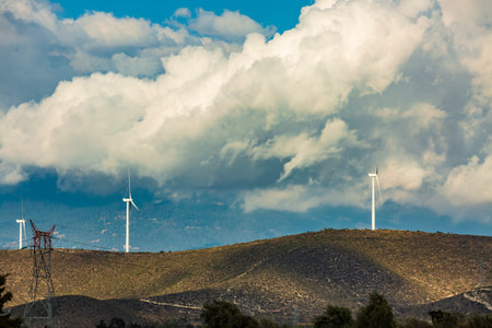 Wind farm. Among farms and hills, wind turbines emerge as a symbol of clean energy, converting the kinetic energy of the wind into electricity.の写真素材