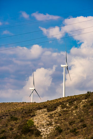 Wind farm. Among farms and hills, wind turbines emerge as a symbol of clean energy, converting the kinetic energy of the wind into electricity.の写真素材