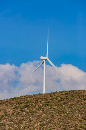 Wind farm. Among farms and hills, wind turbines emerge as a symbol of clean energy, converting the kinetic energy of the wind into electricity.の写真素材